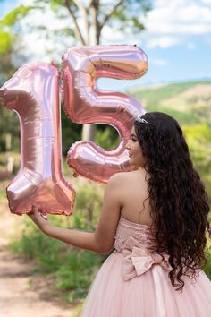 a woman in a pink dress holding up a large number five balloon with the number fifteen on it