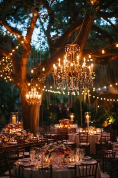 an outdoor wedding reception with chandeliers and tables set up for dinner under the trees