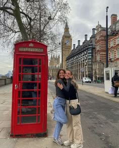 two women hugging each other in front of a red phone booth on the street with big ben in the background