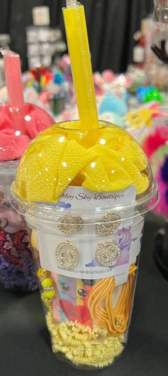 a plastic cup with a yellow straw sticking out of it's top and some other items in the background