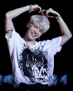 the young man is holding his hair in one hand and smiling at the camera while wearing a t - shirt with graffiti on it