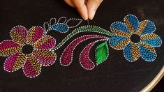 a woman is stitching flowers on a black cloth with colored thread and beading