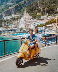 a man and woman riding on the back of a yellow scooter down a road