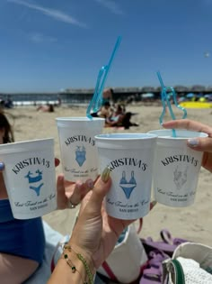 three cups of ice cream are held up in the air by two women at the beach