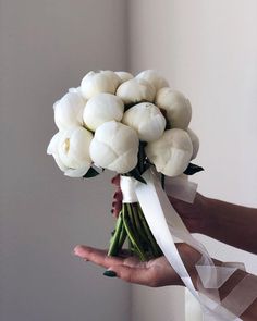 a woman holding a bouquet of white tulips in her hand with a ribbon around it