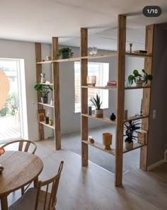 a dining room table and chairs in front of a book shelf with plants on it