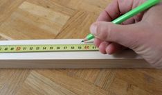 a person is holding a pencil and measuring the length of a piece of wooden plank