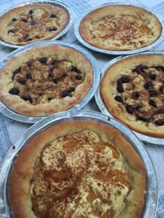 four pies sitting on top of metal pans covered in toppings