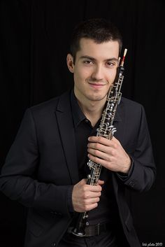 a man in a black suit holding a silver and black flute with strings on it