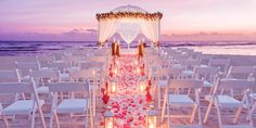 an outdoor wedding set up on the beach at dusk with candles lit in front of it