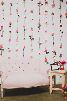 a pink couch sitting in front of a white wall with flowers hanging from it's sides