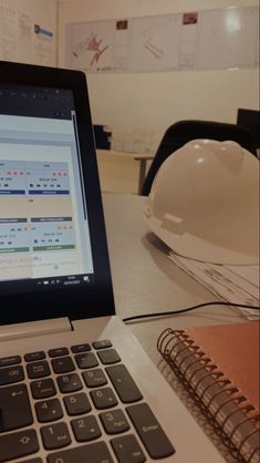 an open laptop computer sitting on top of a desk next to a hard hat and notebook