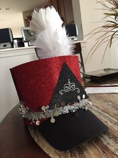 a red and black hat with white feathers on top of a wooden table next to a potted plant