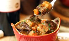 a spoon full of stew with potatoes and carrots in red bowl on green place mat