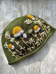 a green knitted hat with yellow flowers on it sitting on top of a wooden surface