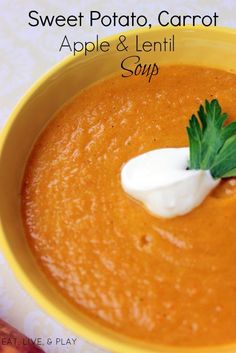 a yellow bowl filled with carrot soup topped with sour cream and green leafy garnish