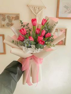 a bouquet of pink tulips is held by someone's hand in front of pictures on the wall