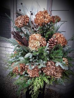 a vase filled with lots of different types of flowers and greenery next to a brick wall