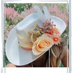 a woman wearing a white hat with flowers and feathers on it's brim