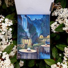 there is a card with a painting on it next to some white flowers and trees