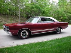 an old red car is parked on the side of the road in front of some trees