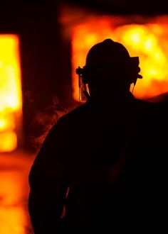 a man standing in front of a fire with his back turned to the camera, wearing a gas mask