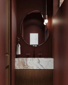 a bathroom with red walls and marble counter tops, along with a round mirror on the wall