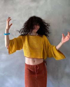 a woman with her arms outstretched in front of a white wall wearing a yellow top and orange skirt