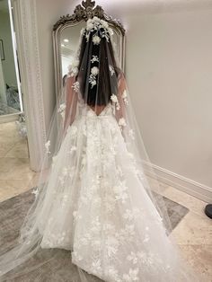 the back of a bride's wedding dress in front of a mirror with flowers on it