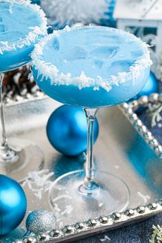 two blue margaritas sitting on top of a silver tray next to christmas ornaments and decorations