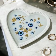 a heart shaped plate with blue and gold eyes on it next to two wedding rings