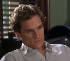 a man with curly hair sitting in an office chair looking off to the side while wearing a white shirt