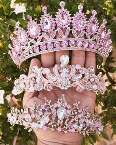 a hand holding three tiaras on top of each other in front of some trees