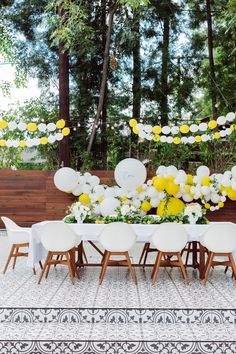 a table set up with white chairs and yellow flowers on the table for a party