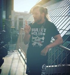 a man with long hair and beard standing on a balcony pointing at his cell phone