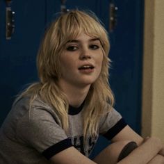 a blonde woman sitting on the floor in front of lockers with her hands crossed