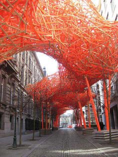 an orange sculpture is in the middle of a street lined with tall buildings and trees