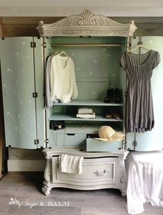 an old fashioned wardrobe with clothes hanging on the door and drawers in front of it