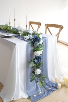 the table is set with blue and white flowers, greenery and candles on it