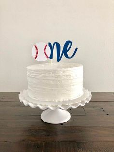 a white cake with a baseball on top and the word one is in blue frosting