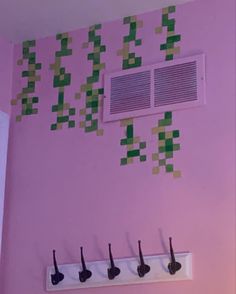 there is a pink wall with green squares on it and four coat hooks in the middle