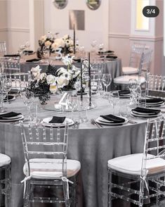 the table is set with silver linens and white flowers in vases, black napkins, and clear chairs