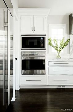 a kitchen with white cabinets and stainless steel ovens, dark wood flooring and black countertops