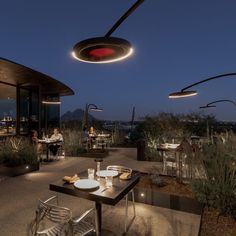 an outdoor dining area at night with people sitting and eating in the distance, surrounded by greenery