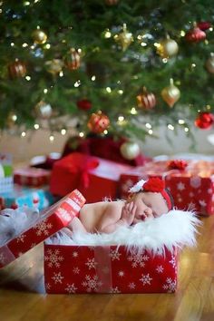 a baby is sleeping in a christmas present box under a tree with presents on the floor