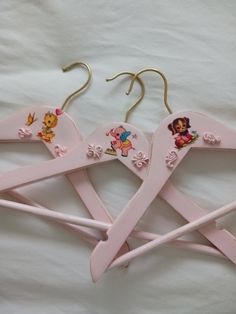 three pink children's wooden clothes hangers with cartoon characters on them, sitting on a white sheet