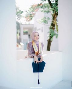 a woman wearing a hijab sitting on top of a white wall next to a tree