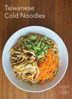 a white bowl filled with noodles and veggies on top of a wooden table