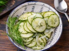 a bowl filled with cucumbers and dill on top of a wooden table