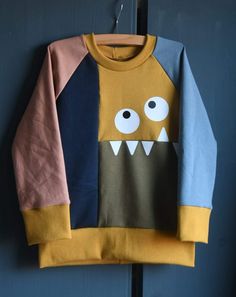 a yellow and blue sweater with an angry face on the front is hanging from a hook